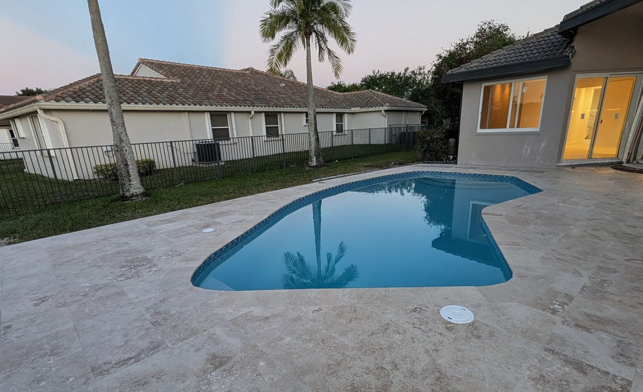 Custom swimming pool with stone deck and waterline tile at dusk - Bravex Trade Services.